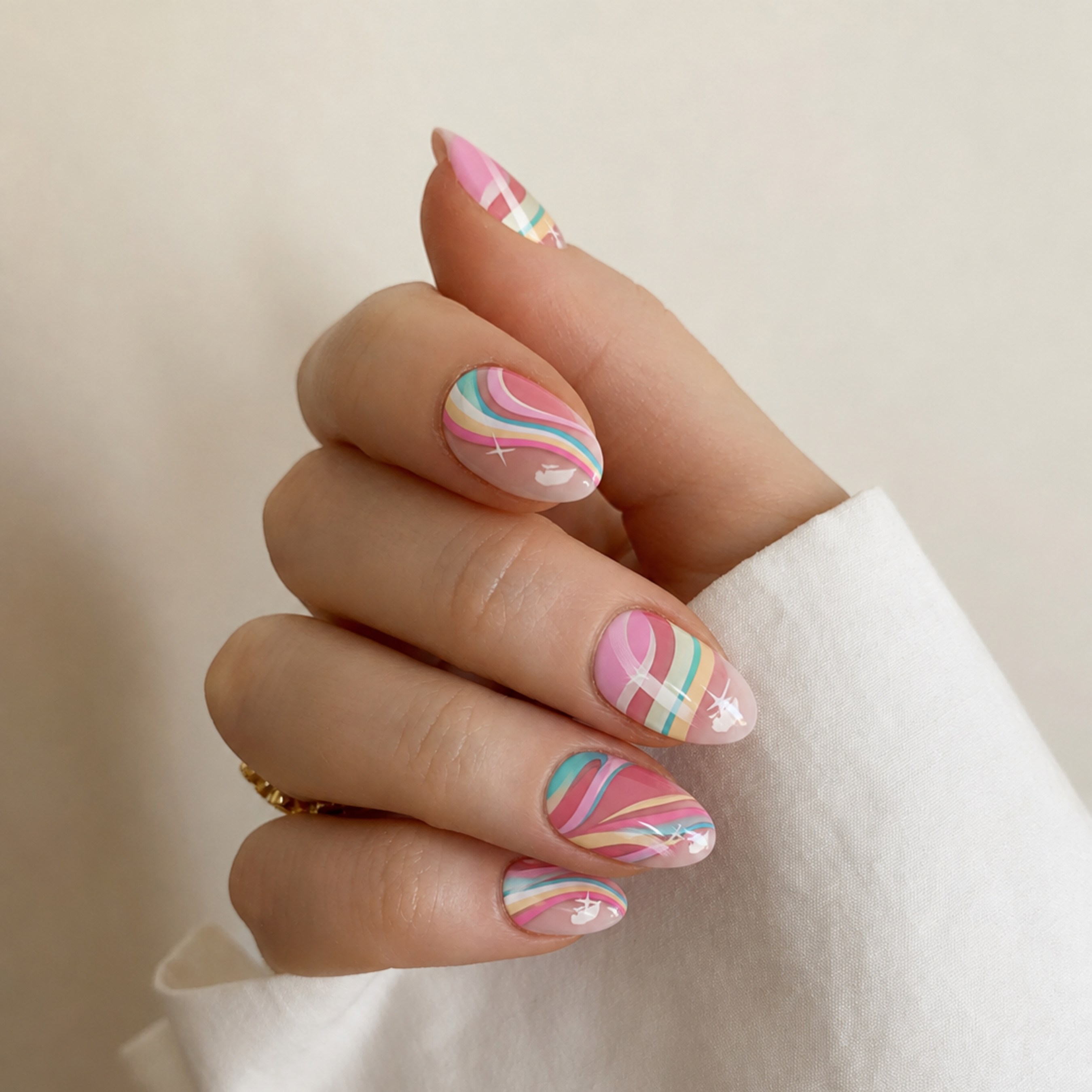 A close-up of a hand with manicured nails featuring pastel rainbow swirl patterns in pink, blue, yellow, and white, wearing a white long-sleeve top against a soft beige background.