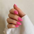 A close-up of a hand with glossy bright pink manicured nails, wearing a white sleeve and a small gold ring, against a soft beige background.