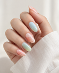 A close-up of a hand with almond-shaped nails styled in a pastel ombre gradient transitioning from soft pink to mint green, with delicate white floral line art painted near the tips, wearing a white long-sleeve top.